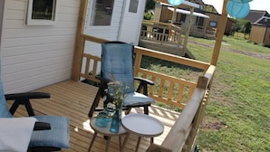 Een houten terras met een tafel en stoelen, een kleine tafel met een bloevas, en een overdekt gebied met een houten balustrade.