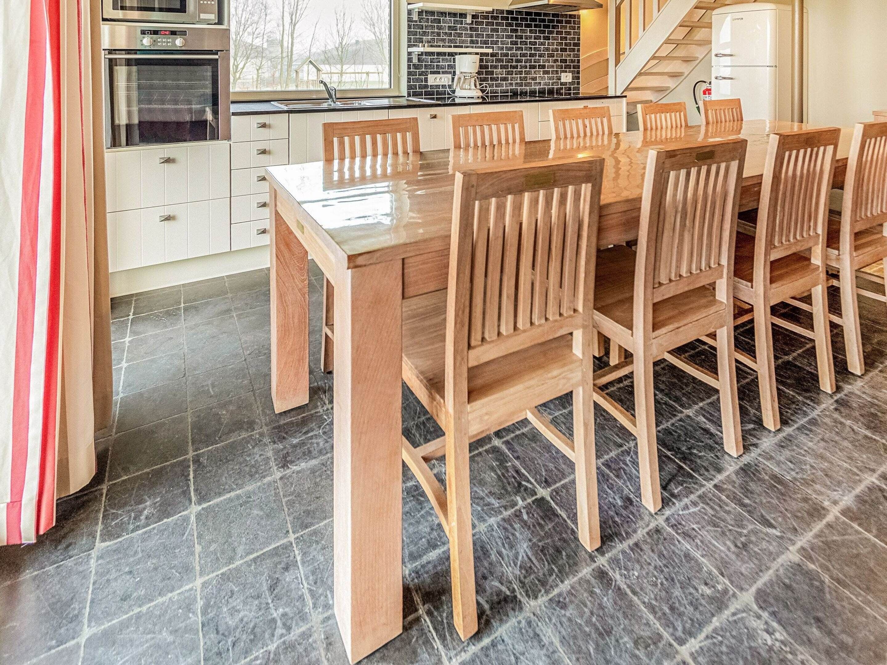 A modern kitchen with a wooden dining table and chairs, a built-in oven, and a black tiled backsplash.