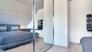 A modern bedroom with a bed, bedside table, mirror, and a sliding door closet. - Modern Holiday Home in De Haan With Garden (De Haan)