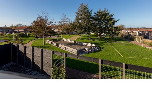 Vista de un parque con un banco de madera, un área de juegos y un césped.