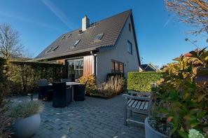 Ein Haus mit Satteldach, einer Terrasse mit Gartenmöbeln und einem gepflegten Garten.