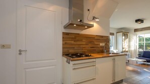 A modern kitchen with a central island, white cabinetry, a wooden backsplash, and a built-in stove. - Attractive Apartment near Center & Beach (Zoutelande)