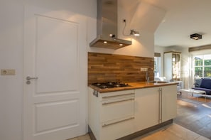 A modern kitchen with a central island, white cabinetry, a wooden backsplash, and a built-in stove. - Attractive Apartment near Center & Beach (Zoutelande)