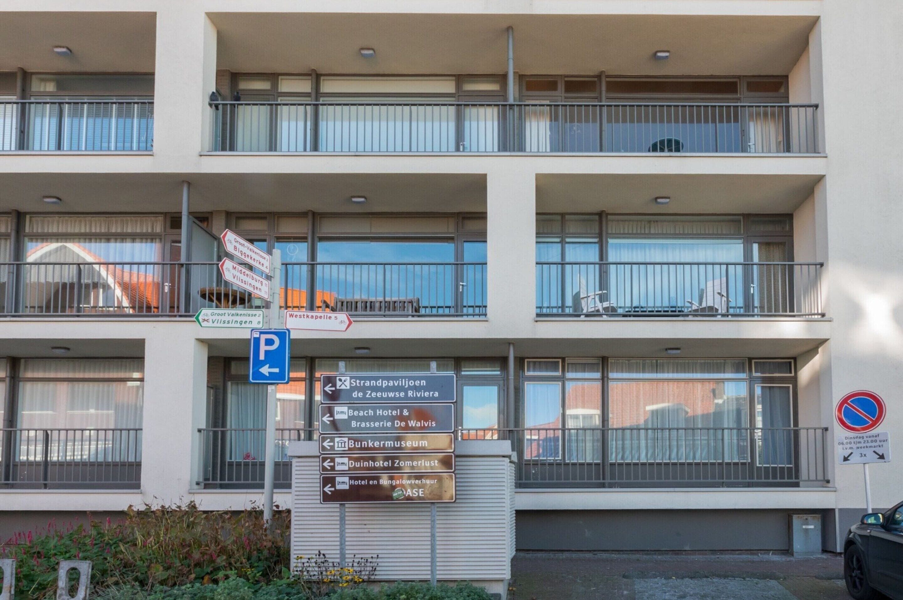 A multi-story building with balconies, a parking sign, and directional signs for various local attractions.