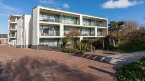 A multi-story residential building with balconies, a brick pathway, and surrounding greenery. - Romantic Coastal Retreat With Scenic Balcony (Zoutelande)