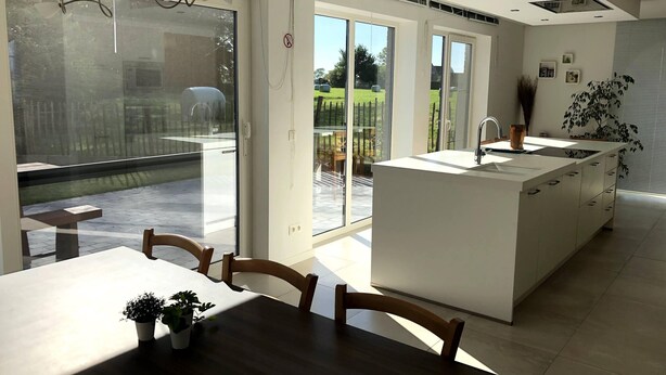 Une cuisine moderne dotée d’un îlot central, de grandes portes-fenêtres coulissantes donnant sur un patio, et d’un coin repas avec une table et des chaises.