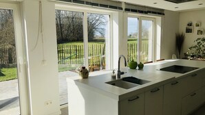 Une cuisine moderne dotée d’un grand îlot central, de deux éviers et offrant une vue sur un jardin grâce à de grandes fenêtres.