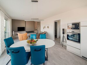 A modern kitchen with a built-in oven and a dining area with a round table and blue chairs.