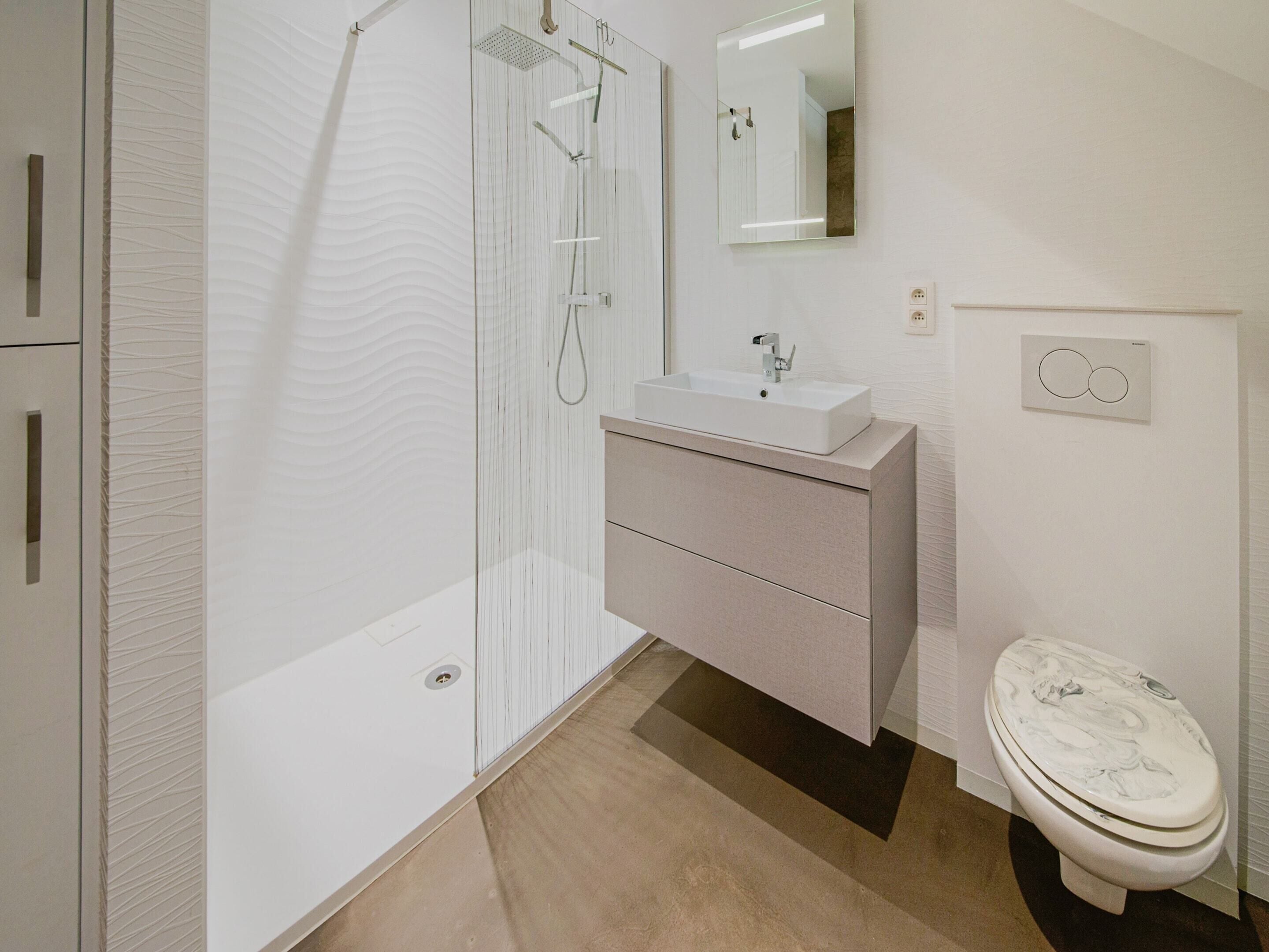 Une salle de bain moderne équipée d’une douche, d’un lavabo, d’un miroir et de toilettes.