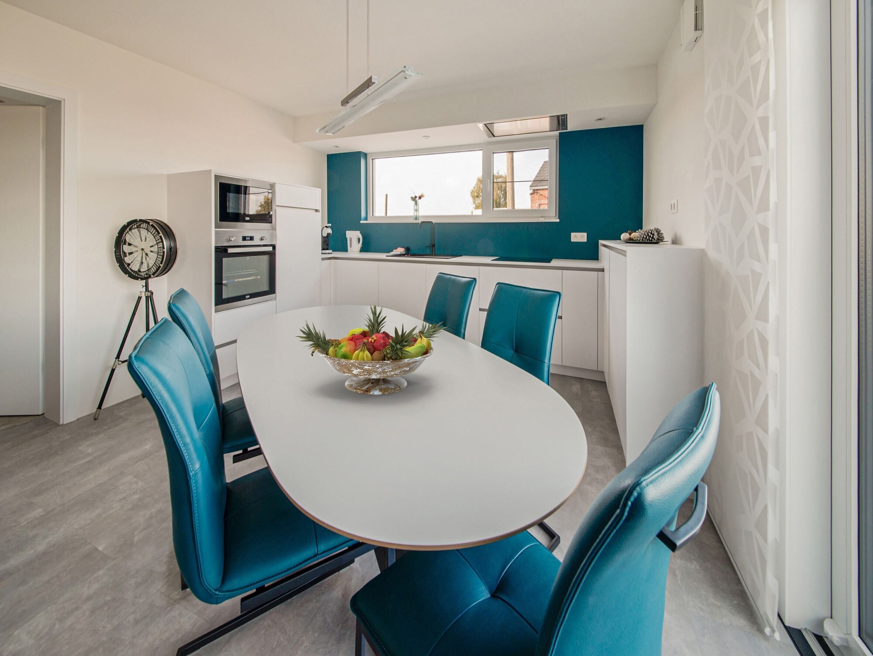 A modern kitchen with white cabinets, a blue accent wall, and a dining area with a white table and blue chairs.