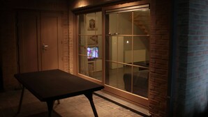 Quarto com porta de vidro deslizante, um banco de madeira e uma televisão ao fundo.