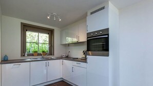 Cozinha moderna com armários brancos, forno embutido e janela com vista para o verde.