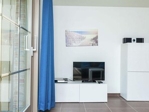 A modern living room with a flat-screen TV on a white cabinet, a painting on the wall, and a sliding glass door with a blue curtain.