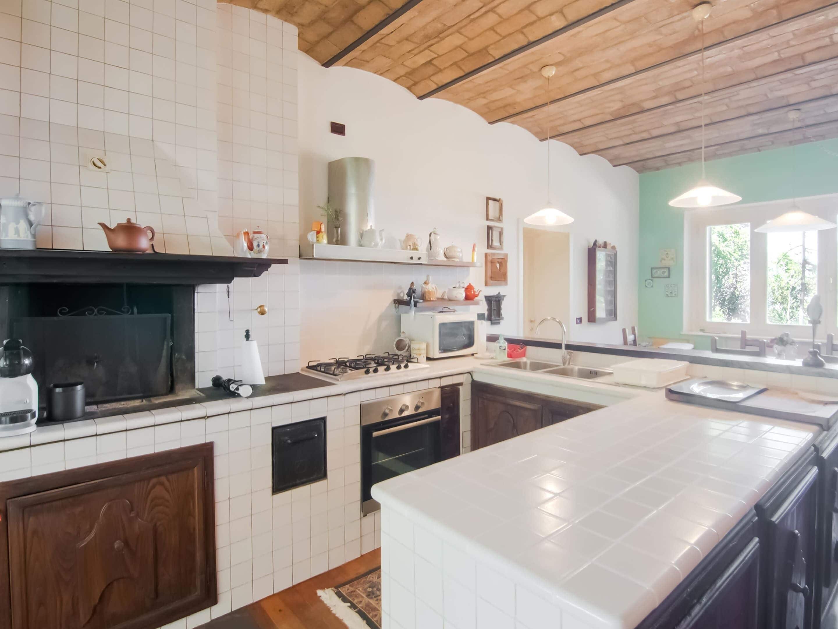 A modern kitchen with white tiles, wooden cabinets, a gas stove, a microwave, and a large island with a sink.