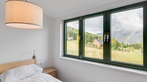 A bedroom with a large window, a bed, a bedside table, and a hanging light fixture. - Apartment in Hohentauern Near Ski Lift (Hohentauern)