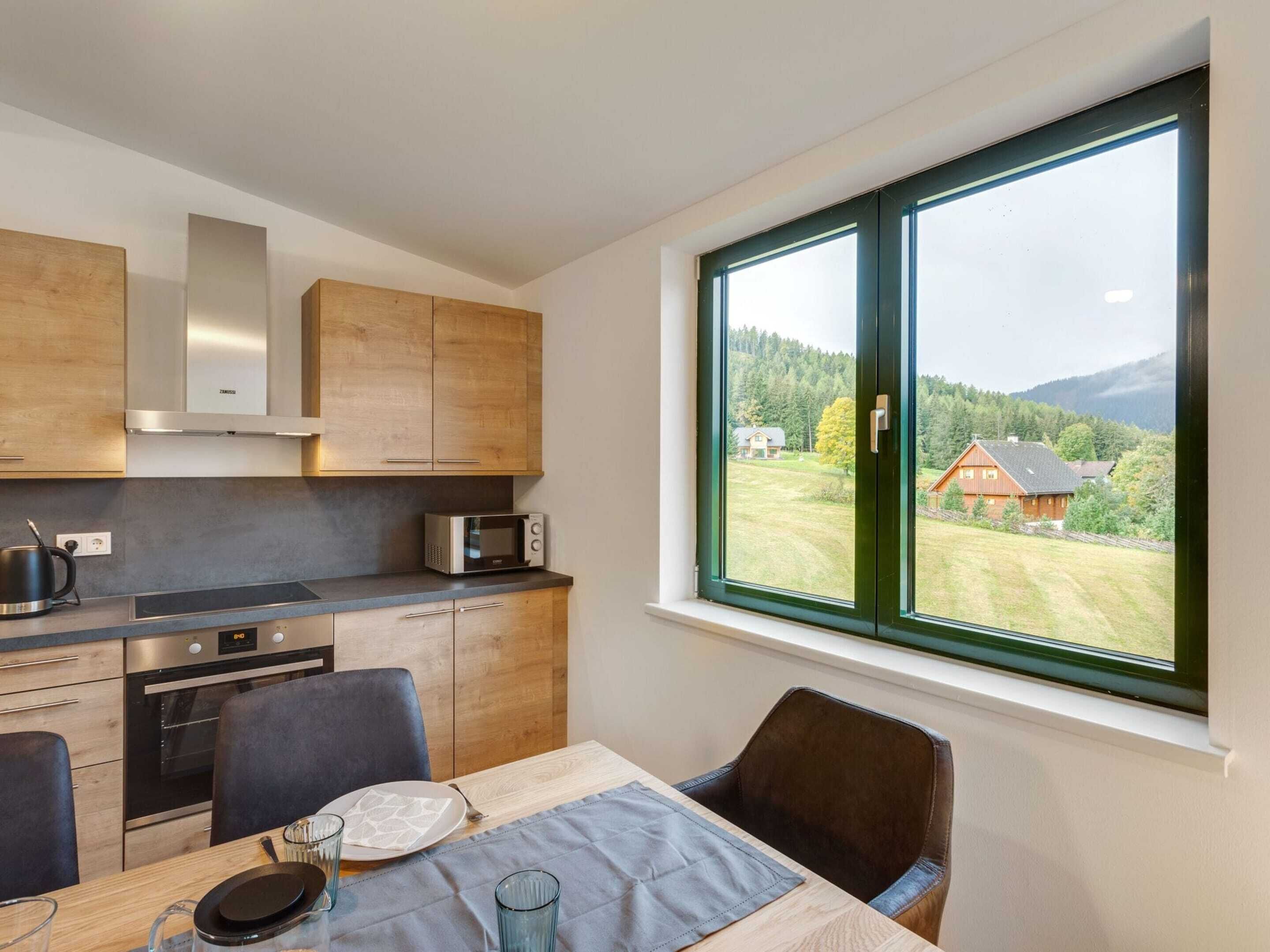 Eine moderne Küche mit Holzschränken, einer eingebauten Mikrowelle und einem großen Fenster mit Blick auf eine ländliche Gegend.