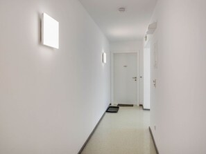 A narrow, white-walled hallway with a door at the end, a small mat on the floor, and a light fixture on the wall. - Apartment in Hohentauern Near Ski Lift (Hohentauern)
