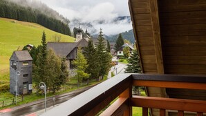 A view from a wooden balcony overlooking a village with traditional buildings, a church, and a road leading to a mountain. - Apartment in Hohentauern Near Ski Lift (Hohentauern)