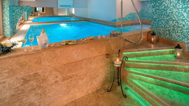 Ein Wellnessbereich mit großem Pool, Whirlpool und einer Treppe mit grüner Beleuchtung.