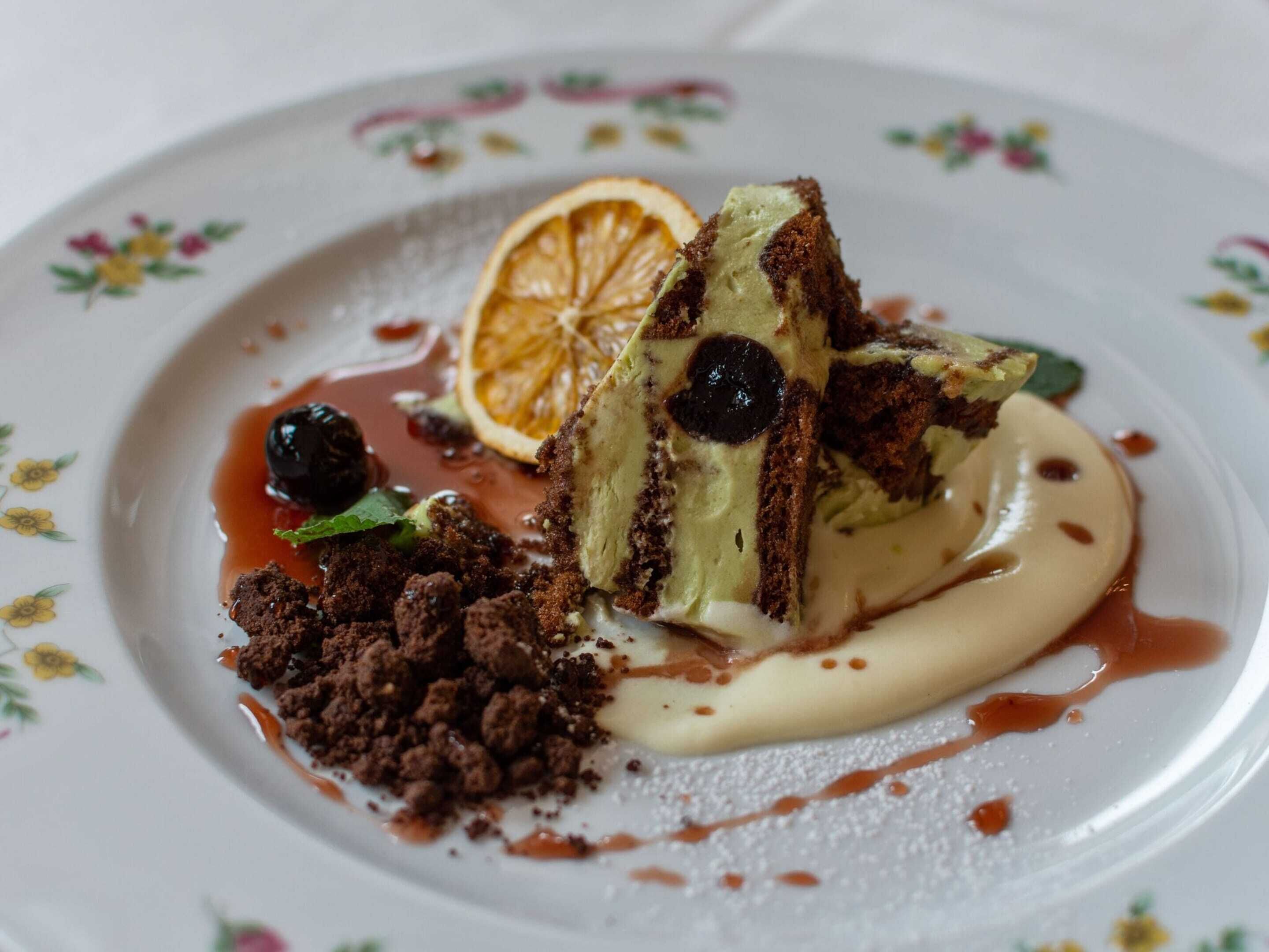 Uma sobremesa com uma fatia de bolo, um pouco de creme e um fio de molho sobre um prato com padrão floral.