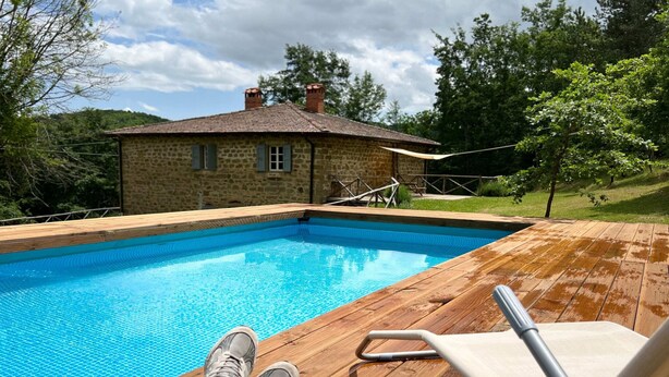 A wooden deck with a pool, a lounge chair, and a stone building in the background. - Belvilla by OYO Villa Pian di Fiore (Pratovecchio Stia)