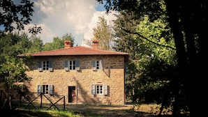 A stone house with a tiled roof, surrounded by trees and a grassy yard. - Belvilla by OYO Villa Pian di Fiore (Pratovecchio Stia)