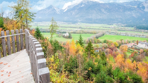 Une plateforme d’observation en bois surplombe une vallée aux couleurs automnales et offre une vue sur des montagnes lointaines.