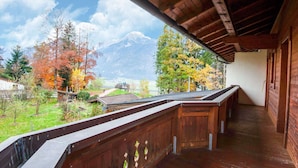 Un balcon en bois offrant une vue sur un paysage montagneux et les couleurs automnales des arbres.