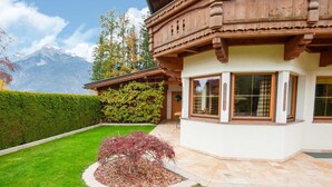 Un chalet traditionnel en bois, doté d’une façade en pierre, d’un jardin bien entretenu et surplombant un paysage montagneux.