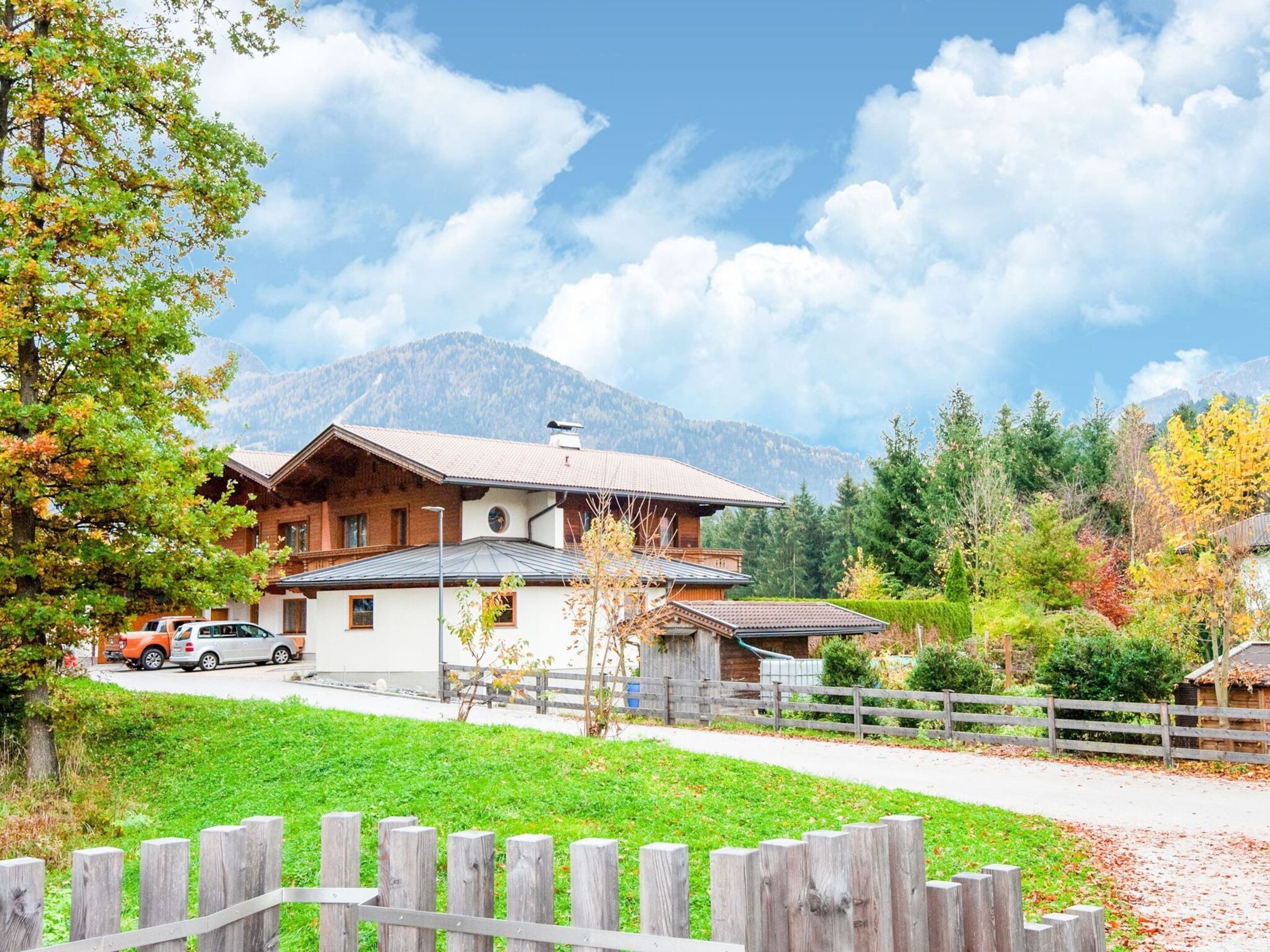 Un chalet traditionnel avec un toit en pente, une clôture en bois au premier plan et un paysage montagneux en arrière-plan.