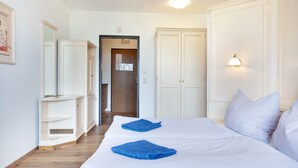 Ein Hotelzimmer mit einem großen Bett, zwei blauen Handtüchern, einem Kleiderschrank, einem Spiegel und einer Tür zu einem Flur.