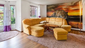 A modern living room with a yellow sectional sofa, a glass coffee table, and a large leopard painting on the wall. - Ruhige Gartenwohnung in Dresden (Dresden)