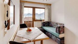 A cozy room with a wooden table, a bowl of fruit, a sofa, and a window with a view of mountains. - Peaceful Apartment in Fügenberg near Ski Area (Fuegenberg)