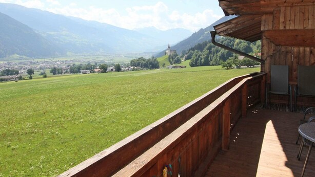 A wooden balcony with a view of a green field, a distant church, and mountains. - Peaceful Apartment in Fügenberg near Ski Area (Fuegenberg)