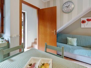 A room with a dining table, a sofa, a clock, and a door leading to a staircase. - Belvilla by OYO Trilocalescarlino (Scarlino)