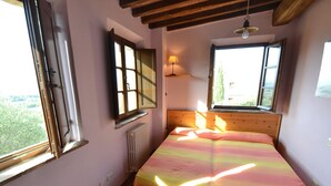 Une chambre avec un lit en bois, une fenêtre donnant sur un beau paysage, un radiateur et une petite table en bois.