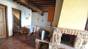 Une cuisine rustique avec une cheminée en pierre, un coin repas avec une table et des chaises, et un lave-linge placé dans un coin.