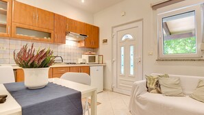A compact kitchen with wooden cabinets, a microwave, and a dining area with a table and chairs. - Apartment in Medulin Near the Beach (Medulin)