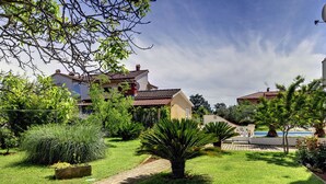 A well-maintained garden with a paved pathway, lush greenery, and a pool area. - Apartment in Medulin Near the Beach (Medulin)