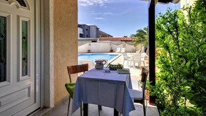 A covered outdoor seating area with a table and chairs, overlooking a swimming pool and a building with a tiled roof. - Apartment in Medulin Near the Beach (Medulin)