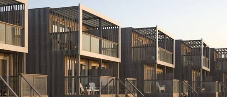 A modern beachside building with multiple balconies, glass windows, and wooden railings.