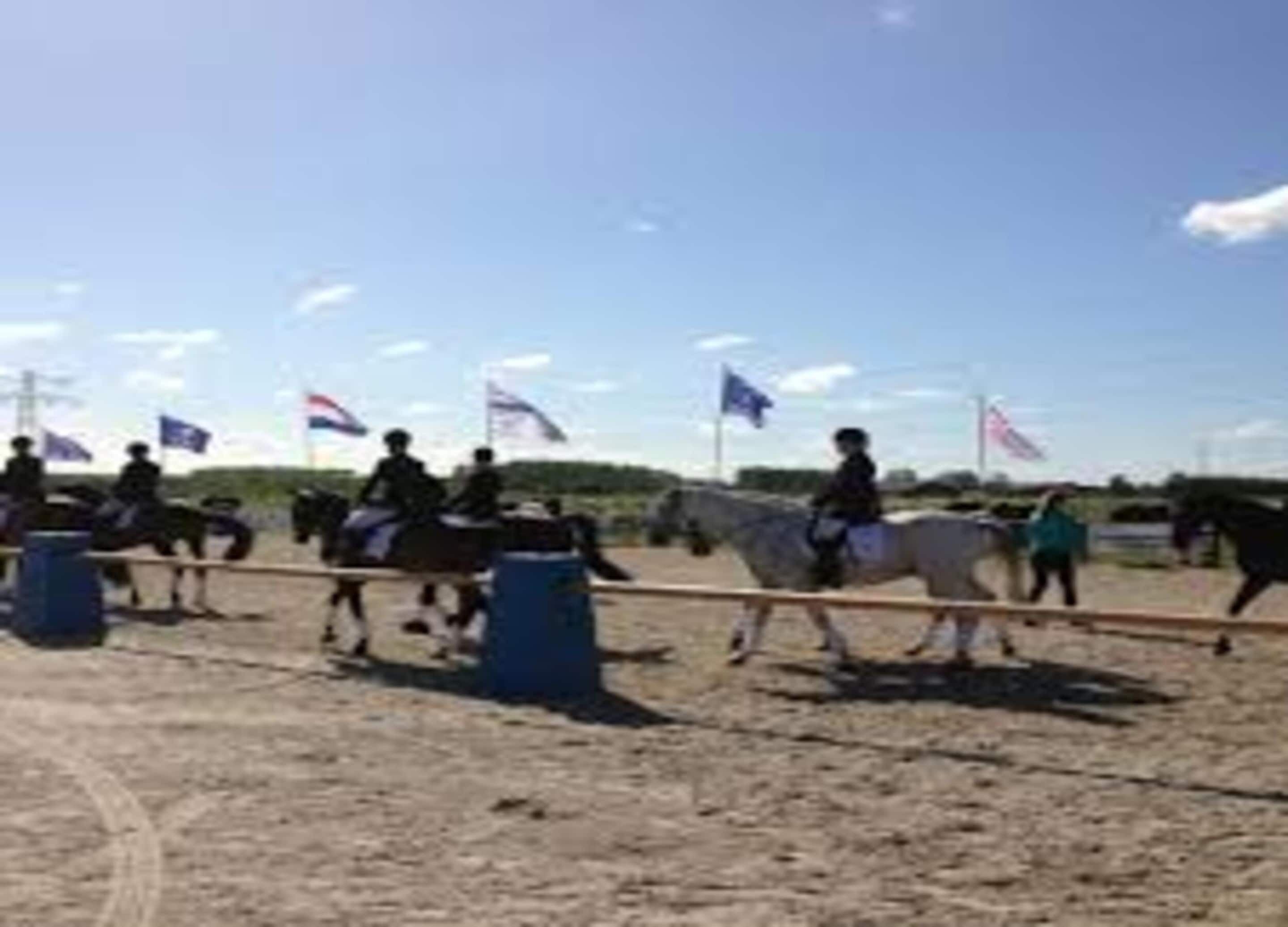 A group of people riding horses in an outdoor arena with flags and barriers.