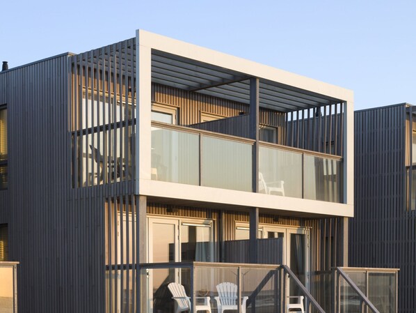 A modern two-story building with a balcony and outdoor seating area. - Beach House in a Dream Location on the Beach (Hoek van Holland)