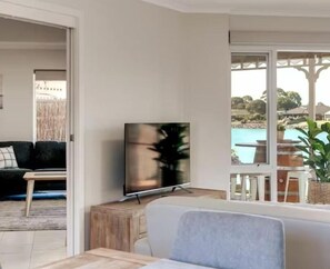A living room with a TV on a wooden stand, a sofa, and a view of a pool and greenery outside.