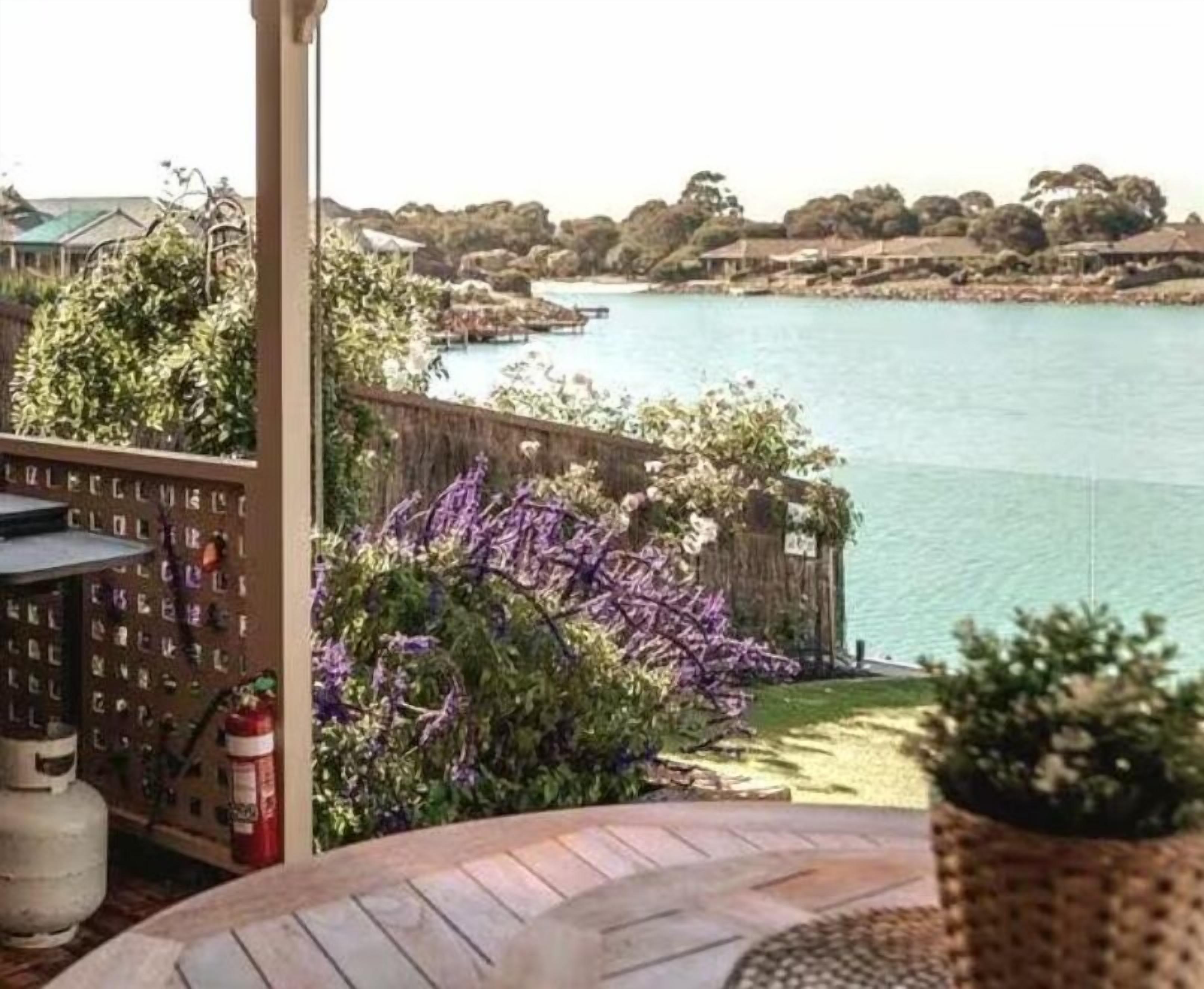 Une vue depuis un balcon donnant sur une étendue d’eau, avec une terrasse en bois, un extincteur et un mur orné d’une grille de lettres.
