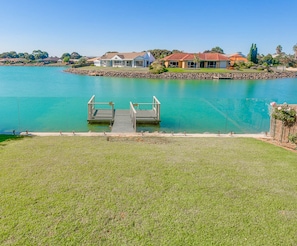 A waterfront property with a dock, grassy areas, and a row of houses.