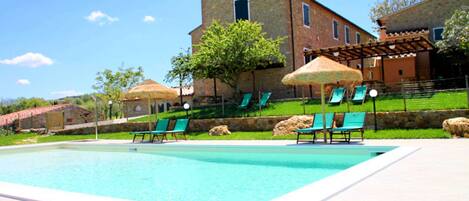 A swimming pool with lounge chairs and umbrellas, a stone building, and a grassy area.