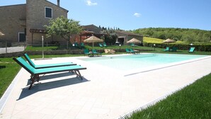 A pool area with lounge chairs, umbrellas, and a stone building in the background. - Belvilla by OYO Tuscan Farmhouse With Private Pool (Montescudaio)