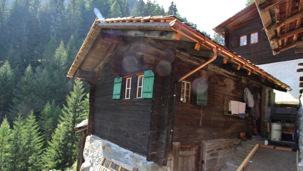 Une cabane rustique en bois, dotée d’un toit à forte pente, de fondations en pierre et d’un porche en bois.