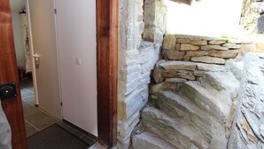 Un mur de pierre jouxtant une porte blanche, avec un cadre de porte en bois et un sol carrelé.